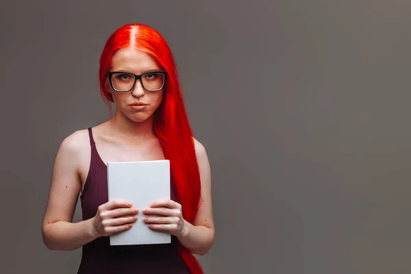Dziewczyna z czerwonymi długimi włosami noszących okulary z białą książką na d — Zdjęcie stockowe