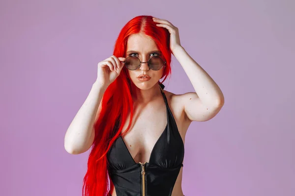 Portret van een meisje met rood lang haar in ronde glazen op een roze — Stockfoto