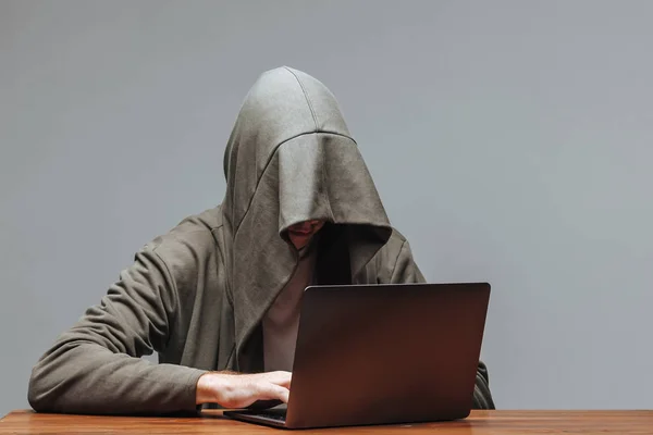 Hacker w kaptur z laptopem na ciemnym tle — Zdjęcie stockowe