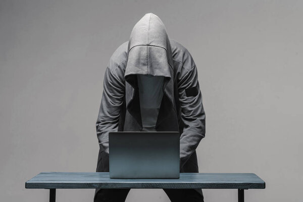 Hacker in a hood with a laptop on a dark background