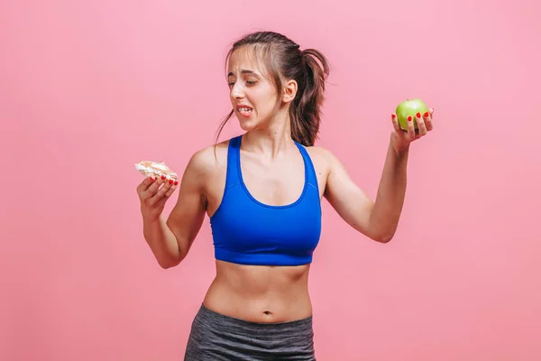 Menina em um fundo rosa segurando um bolo e uma maçã — Fotografia de Stock