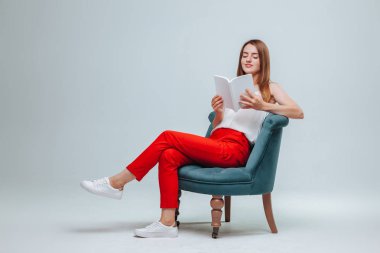 Kırmızı pantolonlu kız bir sandalyede oturan ve bir w ile bir kitap okuma