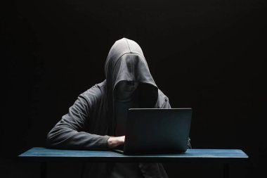 Siyah arka planda dizüstü bilgisayar ile bir kapüşonlu Hacker