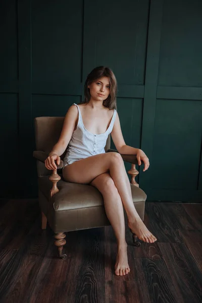Όμορφο κορίτσι με μακριά λεπτά πόδια κάθεται σε μια καρέκλα σε ένα σκοτεινό — Φωτογραφία Αρχείου
