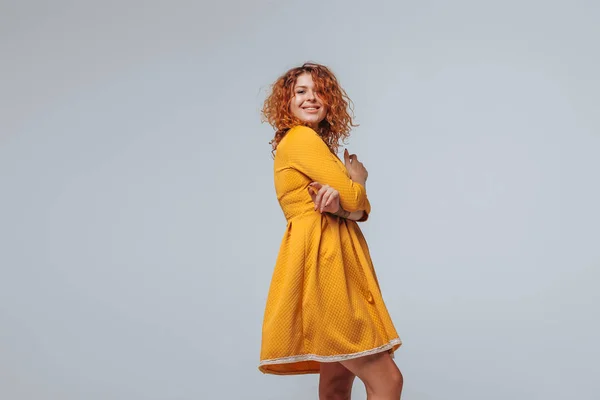 Cheerful red curly girl in a yellow dress on a light gray backgr — Stock Photo, Image