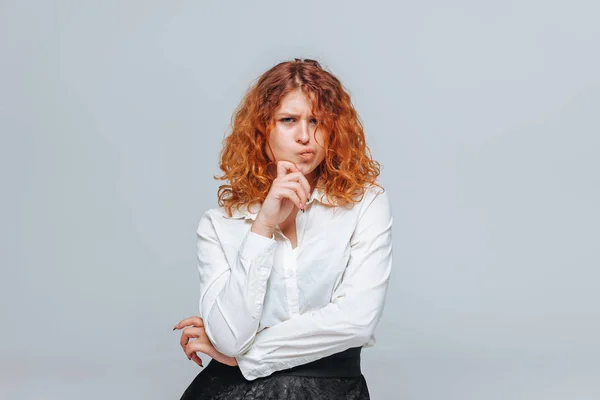 Red headed girl in white shirt thinks on light gray background — Stock Photo, Image