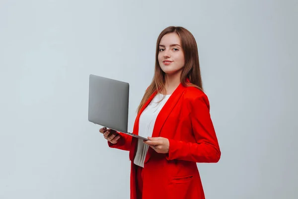 Dziewczyna w czerwonej marynarce trzyma laptopa na jasnym tle — Zdjęcie stockowe