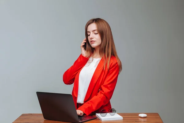 Sekretarz dziewczyna w czerwonej kurtce rozmawiać przez telefon na laptopa — Zdjęcie stockowe