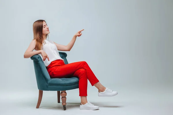 Dziewczyna w czerwonym spodnie siedzi na krześle i punkty na jasnoszary BAC — Zdjęcie stockowe