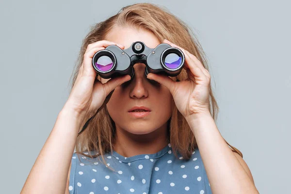 Meisje kijkt door verrekijker op een lichtgrijze achtergrond — Stockfoto