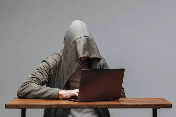 Hacker w kaptur bez twarzy siedzi na laptopie — Zdjęcie stockowe