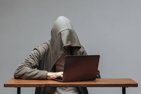 Hacker in a hood without a face sitting at a laptop