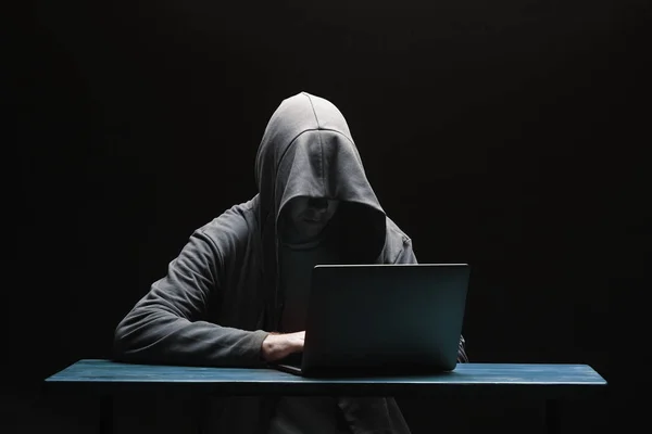 Hacker w kaptur z laptopem na czarnym tle — Zdjęcie stockowe