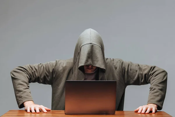 Hacker w kaptur z laptopem na ciemnym tle — Zdjęcie stockowe