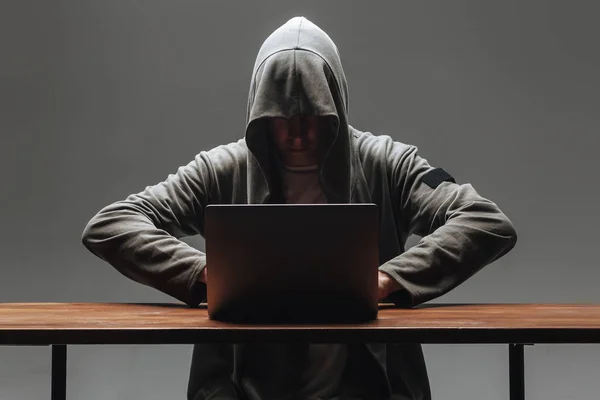 Hacker in a hood without a face sitting at a laptop — Stock Photo, Image