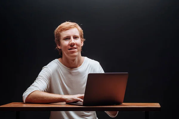 Programmierer in weißem T-Shirt auf schwarzem Hintergrund mit Lapto — Stockfoto