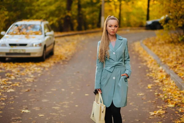 Girl a coat and a bag is on the autumn road — ストック写真
