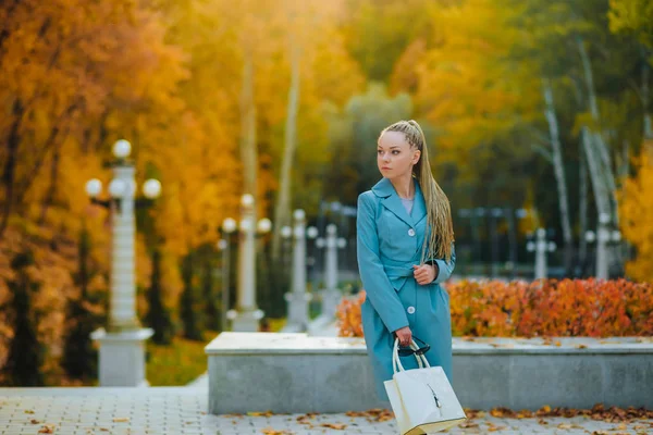 Ragazza che passeggia nel parco in autunno con una borsa bianca in una cioccolata — Foto Stock