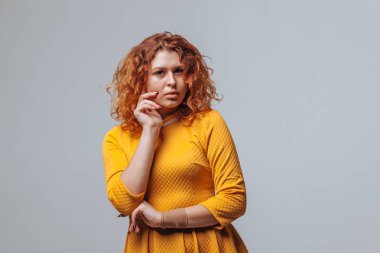 Redhaired kıvırcık kız açık gri bir arka plan üzerinde düşünüyor
