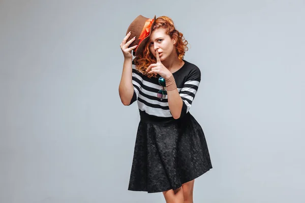 Chica pelirroja posando en un sombrero sobre un fondo gris — Foto de Stock