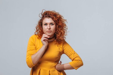 Redhaired kıvırcık kız açık gri bir arka plan üzerinde düşünüyor