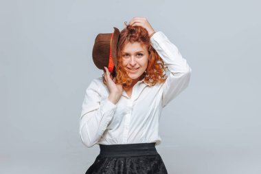 Kahverengi şapkalı kızıl saçlı bir kız gri bir arka plan üzerinde gülümsüyor