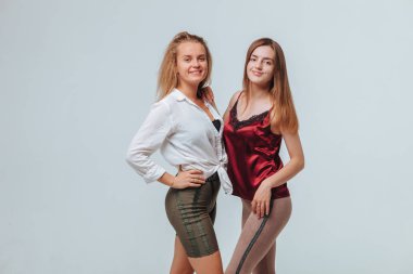 Gri arka planda sarılıp gülen iki kız arkadaş.