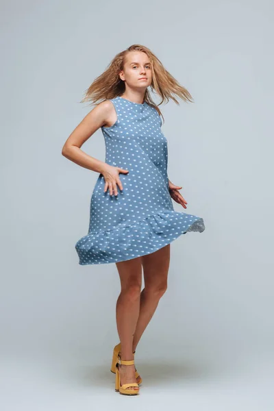 Dívka nosí modré šaty s hráškem na světle šedém pozadí — Stock fotografie