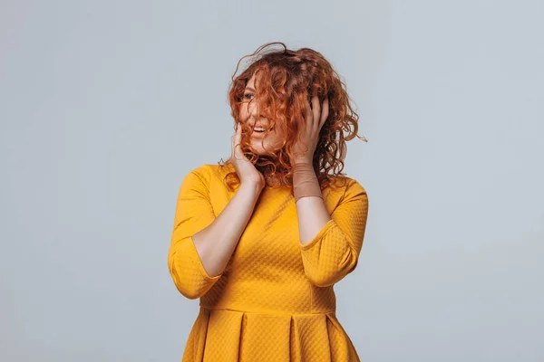 Alegre chica rizada roja en un vestido amarillo en un fondo gris claro — Foto de Stock