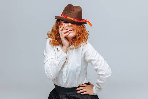 Рыжеволосая радостная девушка в коричневой шляпе на сером фоне
 