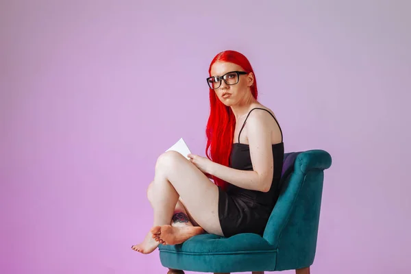 Chica con el pelo largo rojo sentado en una silla y leyendo un libro sobre — Foto de Stock