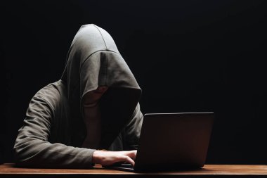 Siyah arka planda dizüstü bilgisayar ile bir kapüşonlu Hacker