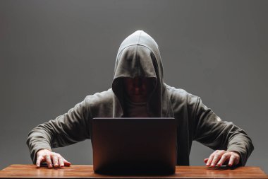 Karanlık bir arka plan üzerinde bir dizüstü bilgisayar ile bir kapüşonlu Hacker