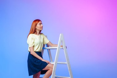 Kızıl saçlı kız mavi-pembe arka planda merdivenleri çıkıyor.