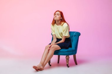 Güzel uzun bacaklı kızıl saçlı kız sandalyede oturuyor.