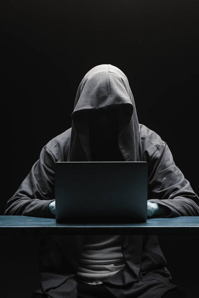 Hacker without a face in a hood with a laptop on a black backgro