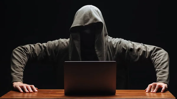 Haker bez twarzy w kapturze z laptopem na czarnym backgro — Zdjęcie stockowe