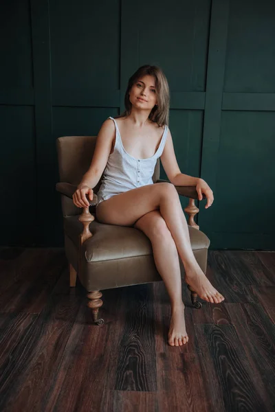 Piękna dziewczyna z długimi cienkimi nogami siedzi na krześle na ciemnym — Zdjęcie stockowe