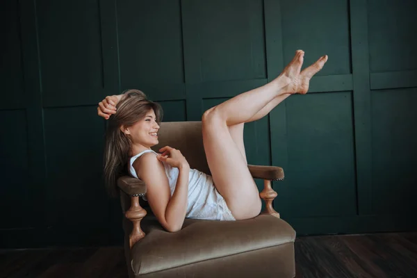 Веселая девушка с длинными тонкими ногами лежит на стуле на темном гри — стоковое фото