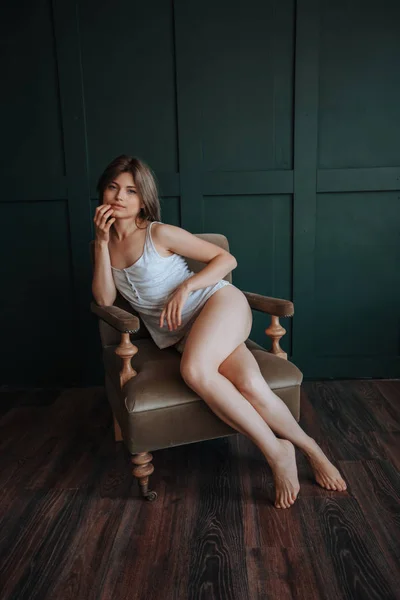 Κορίτσι με γυμνά πόδια κάθεται σε μια καρέκλα σε ένα σκοτεινό φόντο — Φωτογραφία Αρχείου