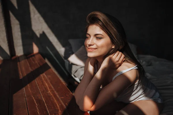 Menina sentada na cama junto à janela sob a luz do sol — Fotografia de Stock