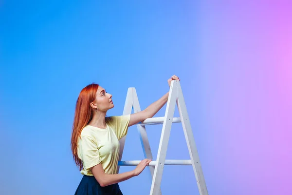 Рыжая девушка поднимается по лестнице на сине-розовом фоне — стоковое фото