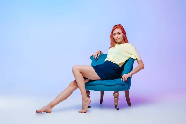 Red-haired girl with beautiful long legs sitting on a chair — Stock Photo, Image