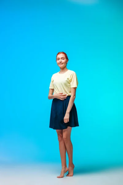 Red-haired girl in a short skirt stands on a blue-green backgrou — Stock Photo, Image