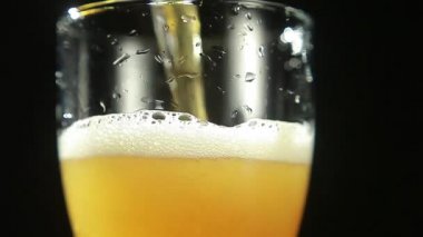 Bira, siyah arka plandaki bir bardağa dökülür. Yakın plan.