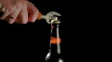 El, siyah arka planda bir bira şişesi açacağını açar.