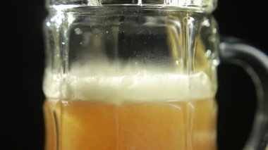 Bira, siyah arka plandaki bir bardağa dökülür. Yakın plan.