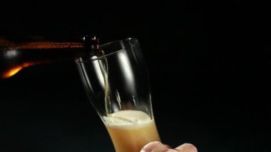 Bira, siyah arka plandaki bir şişeden bardağa dökülür.