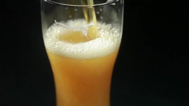 Bira, siyah arka plandaki bir bardağa dökülür. Yakın plan.