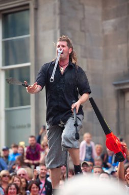 EDINBURGH, SCOTLAND, AUG 5, 2014. Street entertainer balances on unicycle and juggles with burning torch, spanner, and saber on Royal Mile during Edinburgh International Fringe Festival. clipart